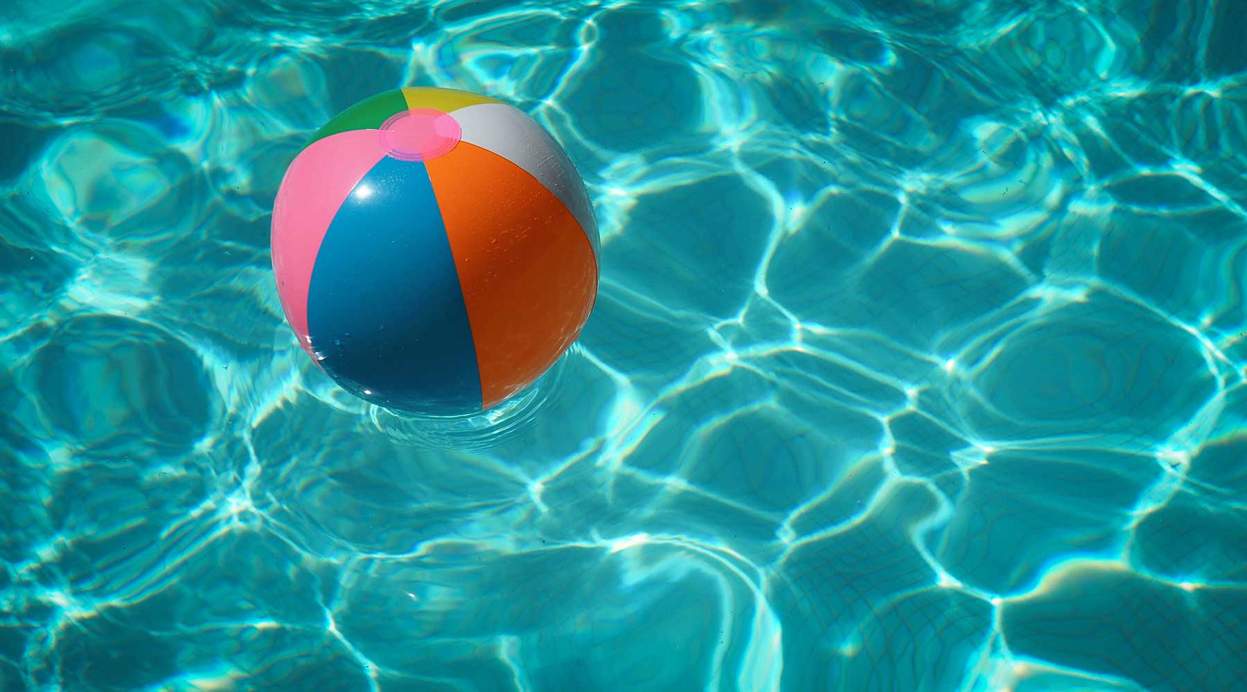 Colorful beach ball floating in a sunlit swimming pool